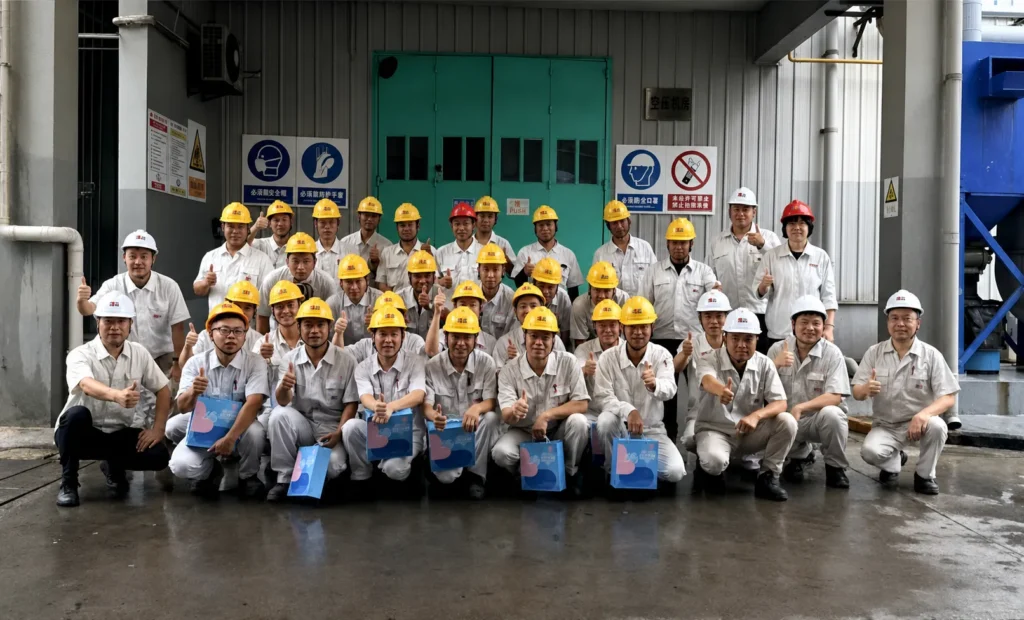 A team of frontline factory workers giving a thumbs-up while holding blue gift bags.