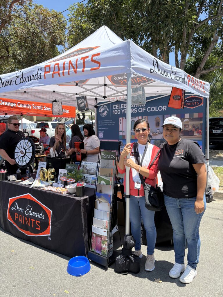 Two women standing in front of a Dunn-Edwards Paints booth displaying colour trends literature.