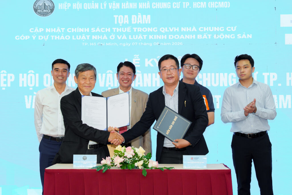 Executives shaking hands and holding signed documents to mark the Ho Chi Minh City Condominium Management Association partnership.