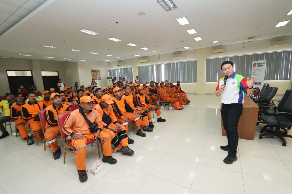 A presenter providing professional painting instruction to municipal maintenance personnel seated in a hall.