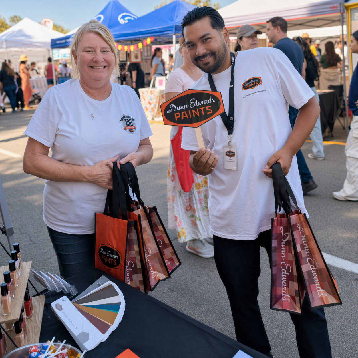 Two smiling employees holding branded shopping bags and a promotional sign at the festival.