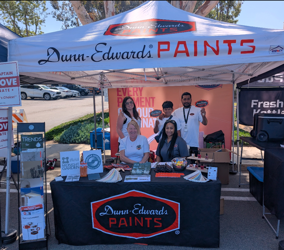 Four employees smiling behind a Dunn-Edwards Paints promotional booth at an outdoor festival.
