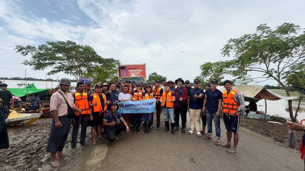 A large group of employee volunteers wearing orange life jackets posing before a relief mission